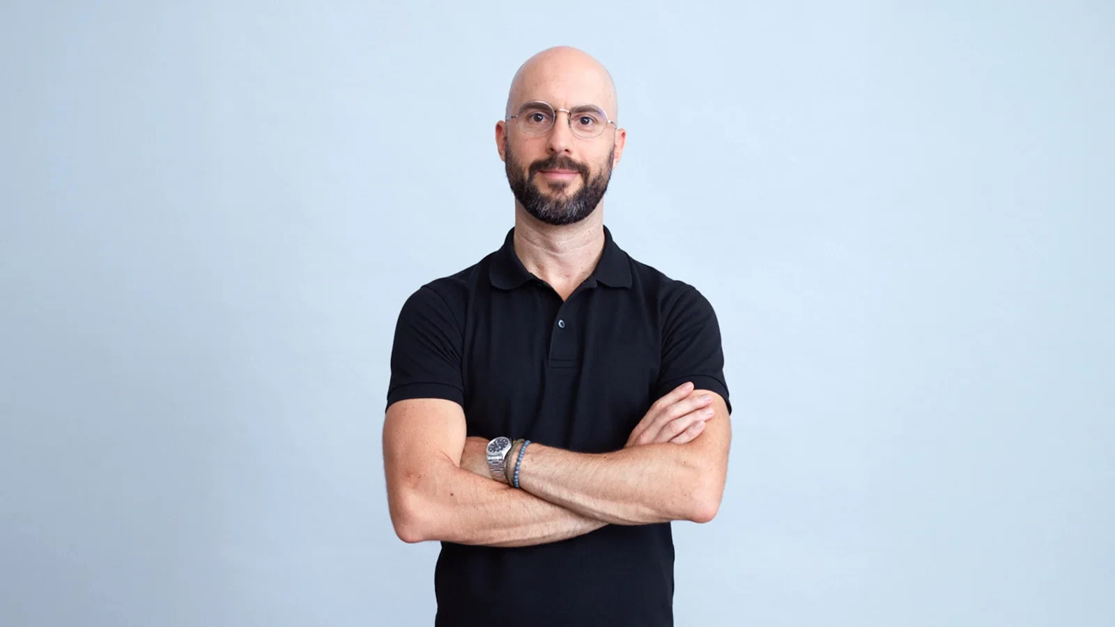 Daniel Posavac, arms folded, against a pale blue backdrop.